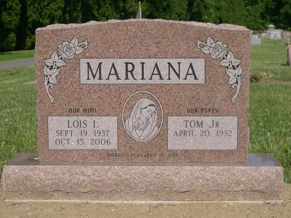 A rose granite upright monument with roses carved at both upper corners, a Madonna relief between two name tablets and a marriage date cut across the foot