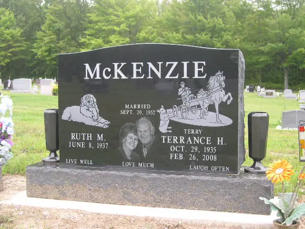 A polished black granite upright monument with an etched dog, a horse-drawn carriage and an oval portrait, with a three-word epitaph across the foot