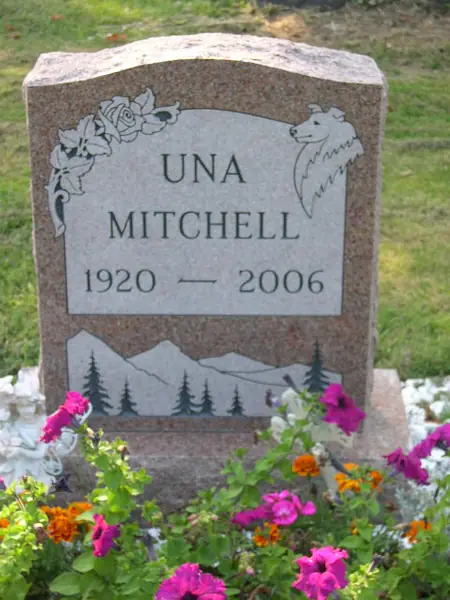 A rose granite upright monument with a rough-hewn top, roses carved at one shoulder and a whale at the other, and the full name and dates in raised lettering