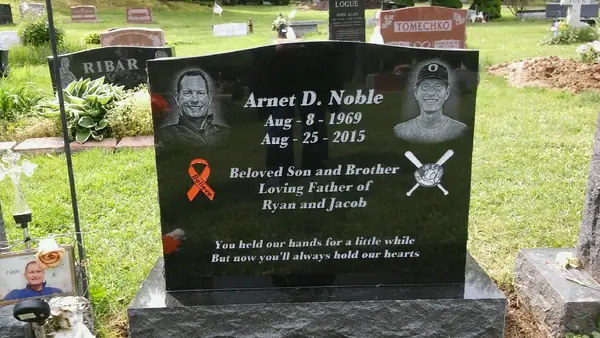 A polished dark grey granite upright monument with two etched portraits, a memorial ribbon, crossed baseball bats and a four-line epitaph
