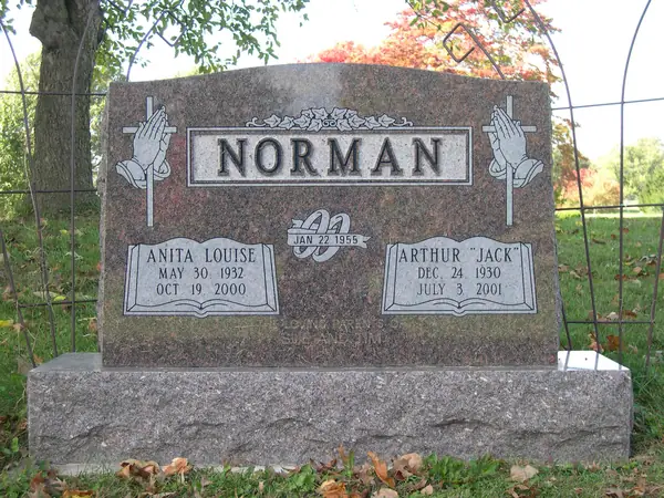A rose granite upright monument with praying hands carved at both shoulders, a raised name panel and a marriage emblem between two name tablets