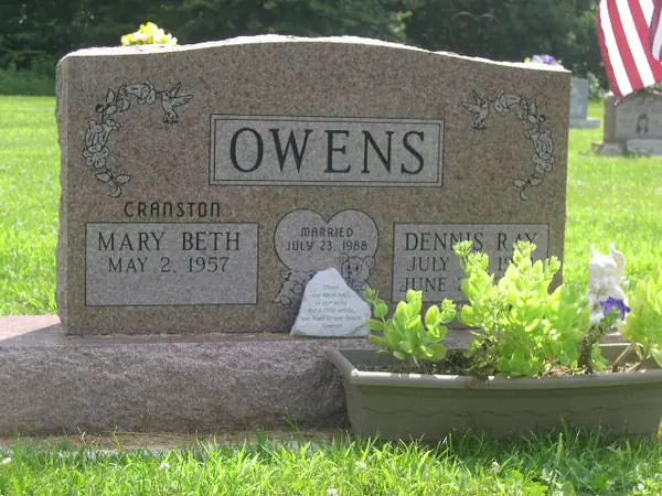 A rose granite upright monument with a rough-hewn top, doves and floral swags carved at both shoulders and a heart-shaped marriage emblem between the name tablets