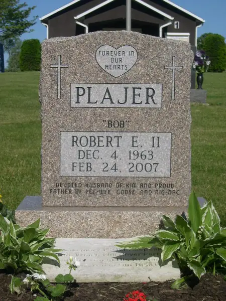 A rose granite upright monument with carved crosses at both shoulders, a heart-shaped epitaph plaque above the raised name panel and a nickname in quotation marks