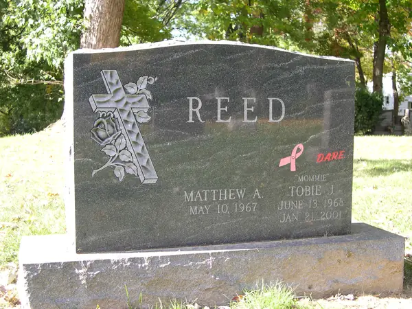 A green-grey granite upright monument with a carved cross wrapped in roses, two name tablets and an etched awareness ribbon