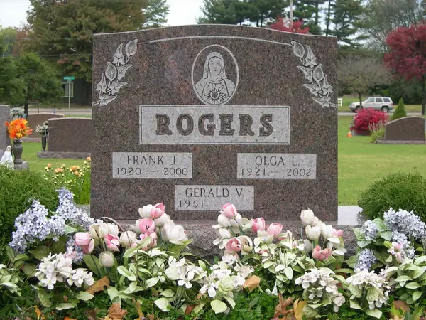 A rose granite upright monument with a Madonna relief above the raised name panel, roses carved at both shoulders and three name tablets