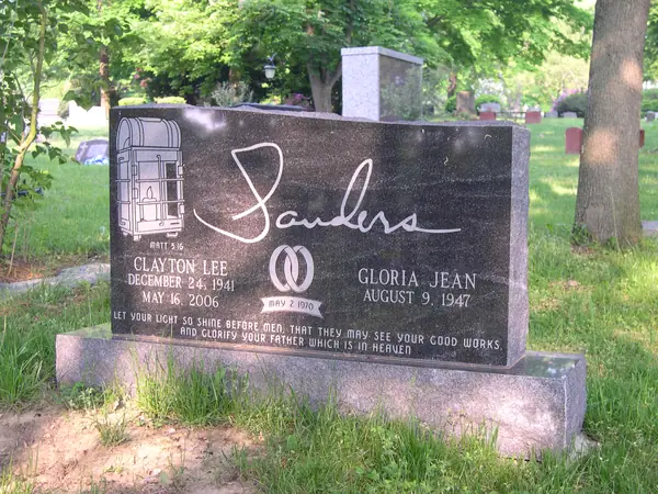 A polished dark granite upright monument with an etched fire engine, the family name in large script, a scripture line and a wedding-ring emblem between the names