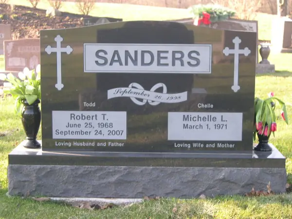 A polished black granite upright monument with carved crosses at both shoulders, a raised name panel, a marriage date banner and relationship lines below the name tablets