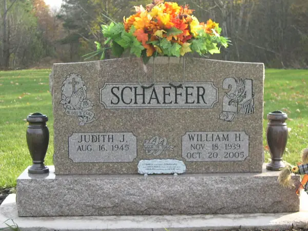 A grey granite upright monument with praying hands carved at one shoulder and a hand holding a rose at the other, with matching bronze vases either side