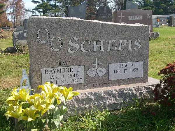 A grey granite upright monument with a rough-hewn top edge, the family name in raised lettering beside carved horseshoes, and a cross between the two name tablets