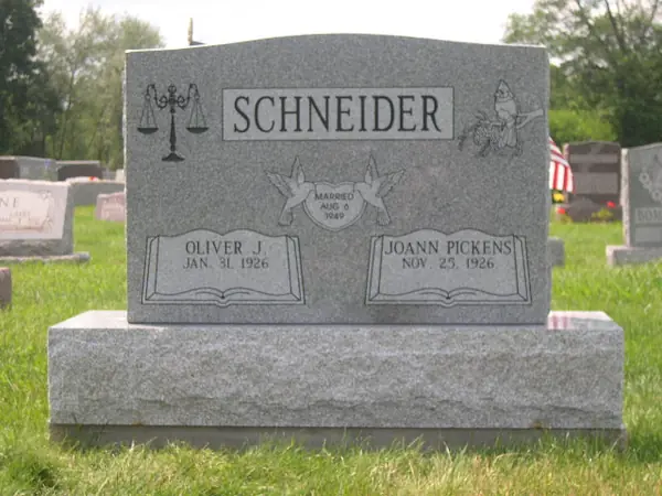 A grey granite upright monument with carved scales of justice at one shoulder and a bird at the other, and open books beneath each name