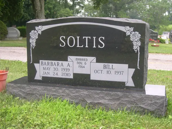 A polished black granite upright monument with roses carved at both upper corners and a marriage-date banner running between the two name tablets