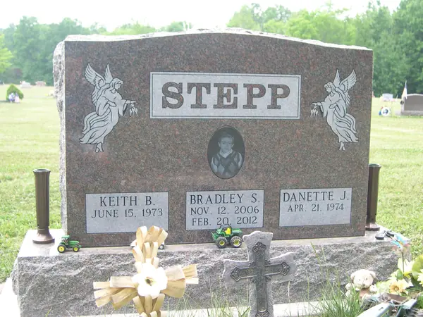 A rose granite upright monument with angels carved at both shoulders, an oval etched portrait of a child and three name tablets