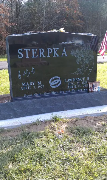 A polished black granite upright monument with musical notes carved at one shoulder, a floral spray at the other and an epitaph line across the foot