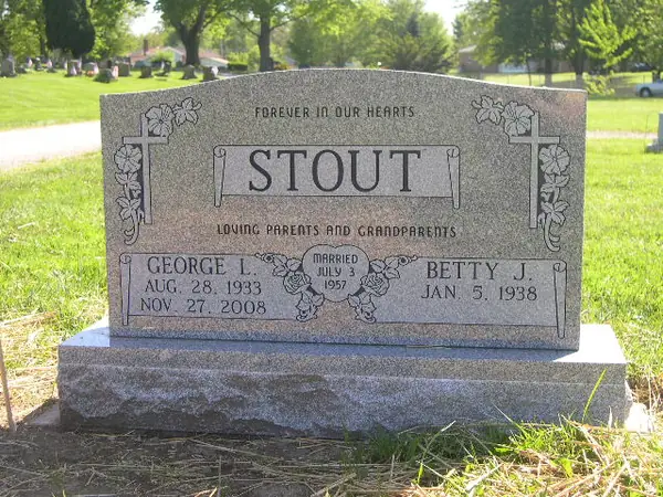 A grey granite upright monument with an epitaph banner above the raised name panel, floral corners and a marriage emblem between the two name tablets