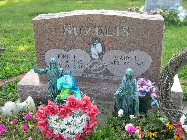 A rose granite upright monument with an oval etched portrait between two carved hearts, a marriage date below and statuary set among the plantings