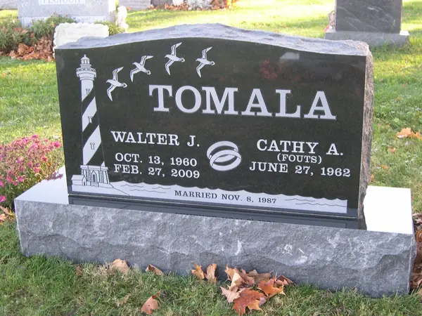 A polished black granite upright monument with an etched lighthouse and gulls, a wedding-ring emblem between the name tablets and a marriage date across the foot