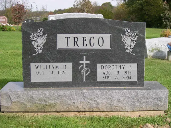 A grey granite upright monument with roses carved at both shoulders, a raised name panel and a cross between the two name tablets