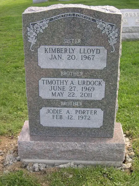 A rose granite upright monument with an epitaph banner across the top, carved flowers at both shoulders and three name tablets labelled by relationship