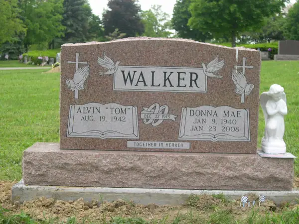 A rose granite upright monument with praying hands and crosses at both shoulders, doves above the name panel, a marriage emblem and an epitaph banner