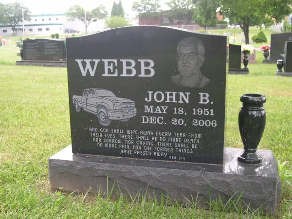 A polished dark granite upright monument with a laser-etched portrait and pickup truck, the family name in raised lettering and a scripture passage across the foot
