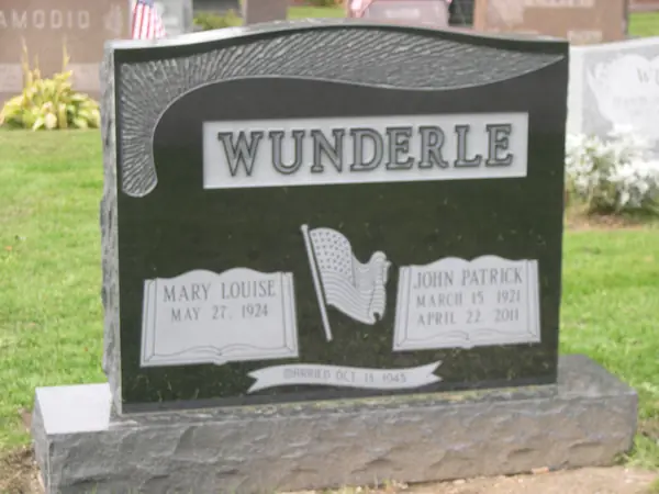 A polished black granite upright monument with a carved furled flag and drape, open books beneath each name and a marriage-date banner across the foot