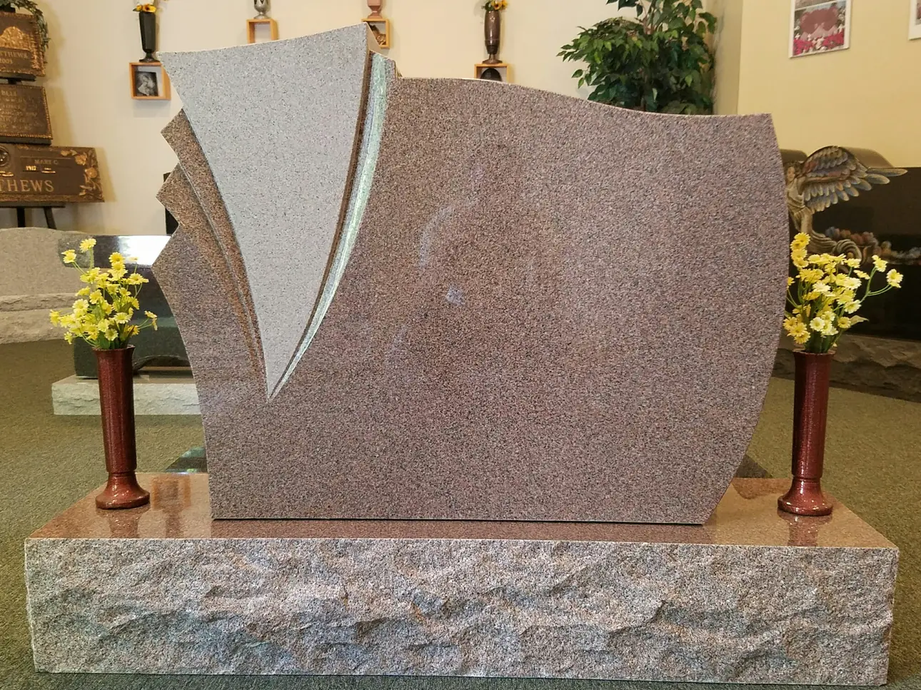 A sculpted monument in cinnamon granite in the AMGC showroom, its polished face beside the rough-hewn base cut from the same stone.