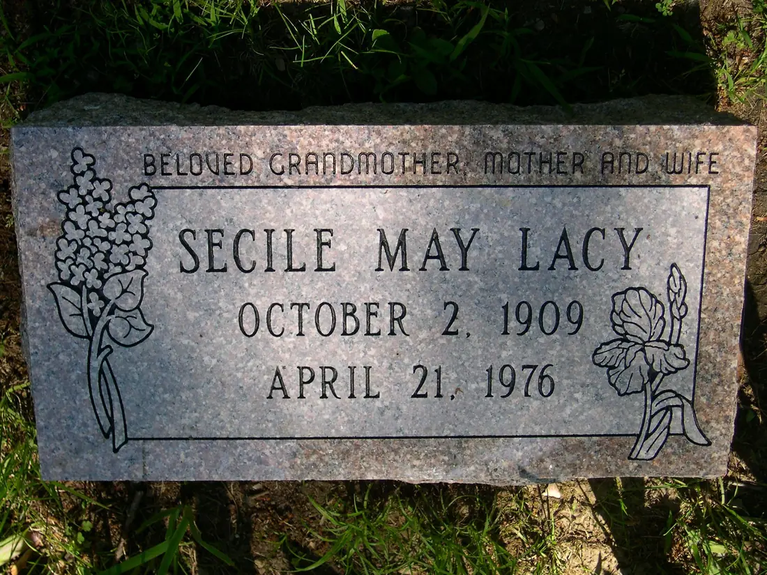 A flat granite marker with the line Beloved Grandmother, Mother and Wife running across the top, a name and two dates below, and lilac and iris carved at either side.