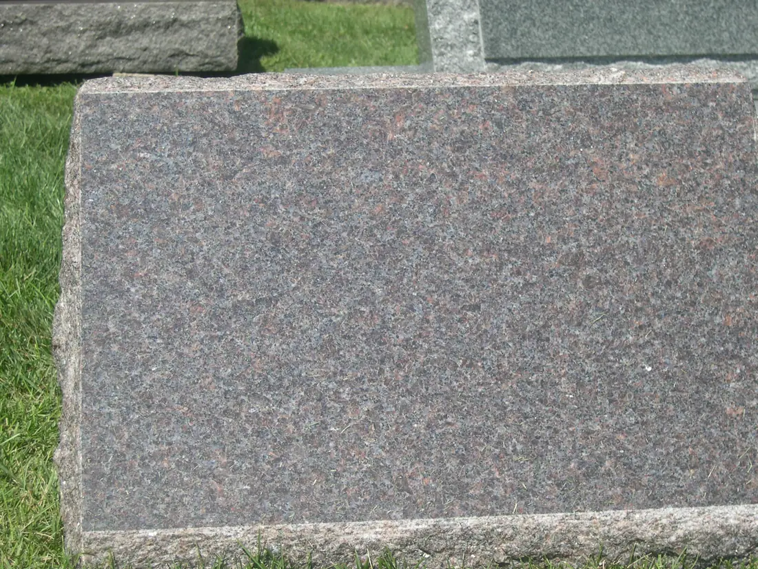 A mahogany granite slab photographed square on, its surface filling the frame so the brown and gray grain reads without reflection.