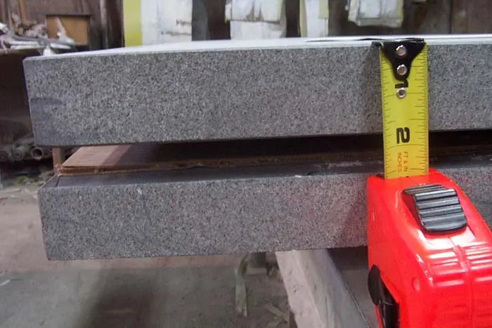 A tape measure held against two granite bases stacked on timber in the workshop, one polished and one with a rough-cut face.