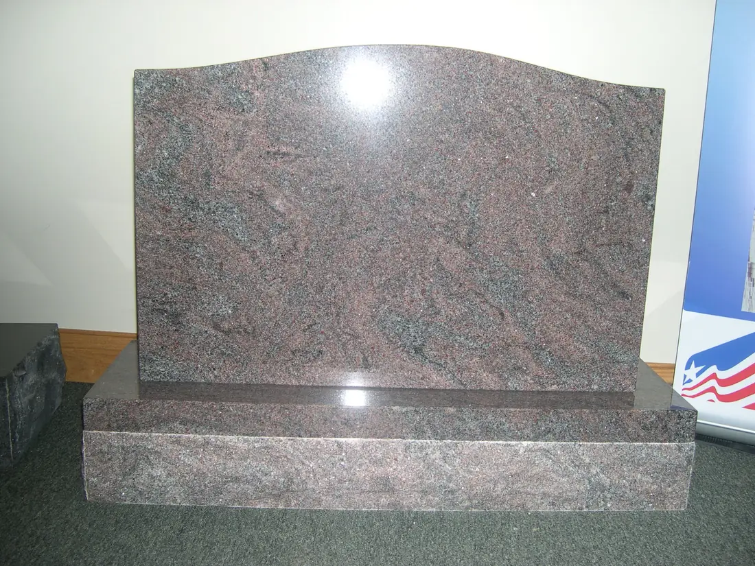 A polished red granite monument whose surface is crossed by broad swirling bands of darker mineral veining.