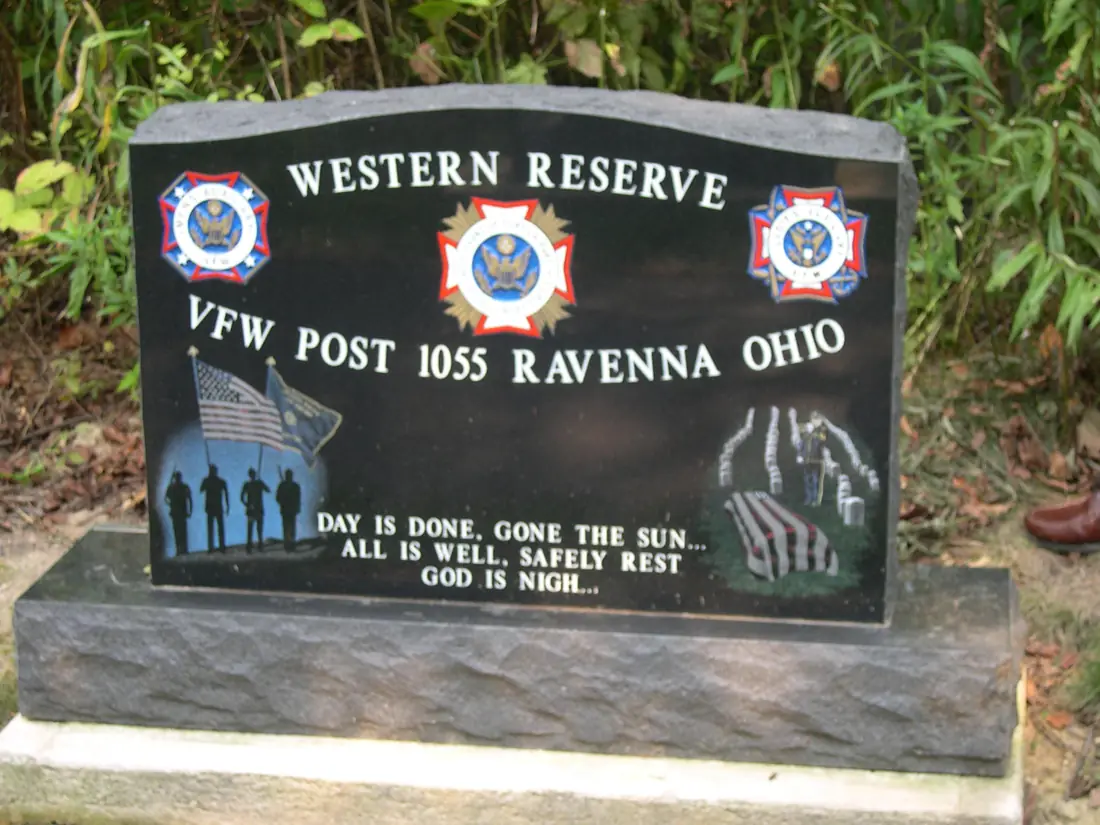 A polished black granite memorial on a rough base reading Western Reserve VFW Post 1055 Ravenna Ohio, with service emblems, etched soldier silhouettes and a flag, above the closing lines of Taps.